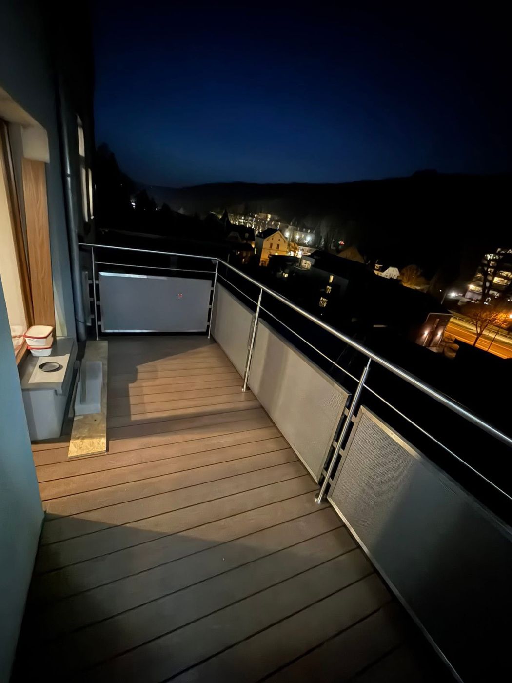 Le même balcon inox au crépuscule, avec vue sur la vallée éclairée
