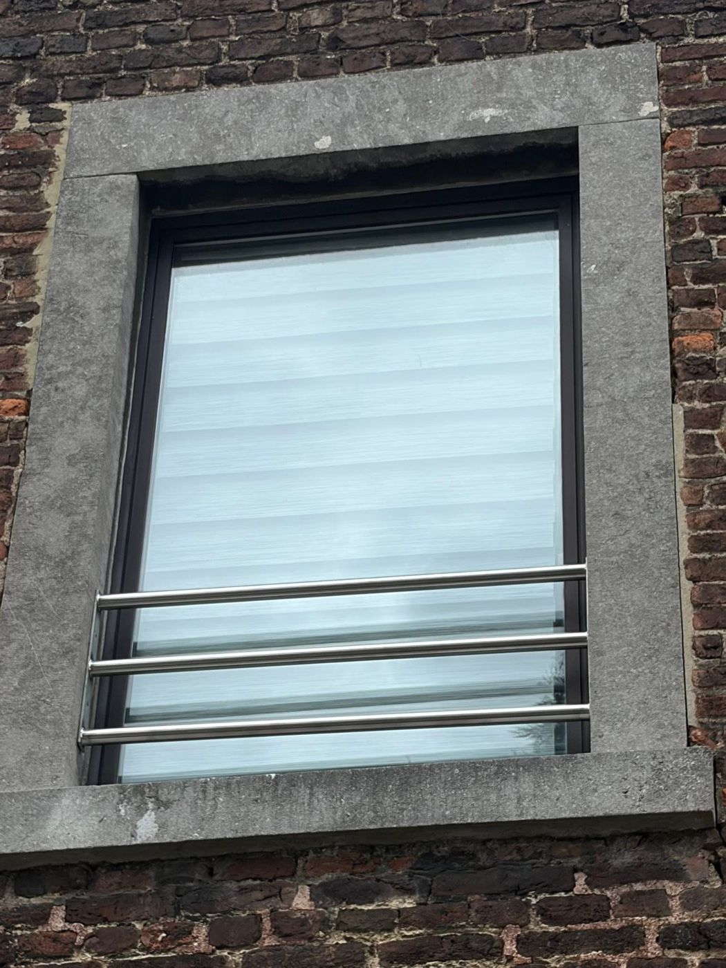 Barre d'appui à trois tubes en inox brossé posée dans l'encadrement en pierre bleue d'une fenêtre