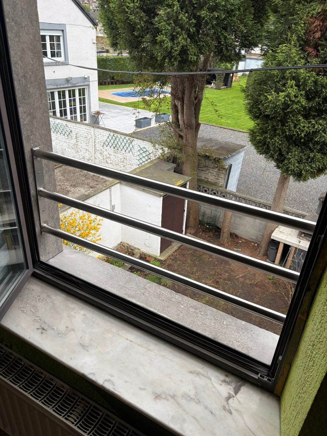 Barre d'appui en inox vue de l'intérieur, fenêtre ouverte sur un jardin