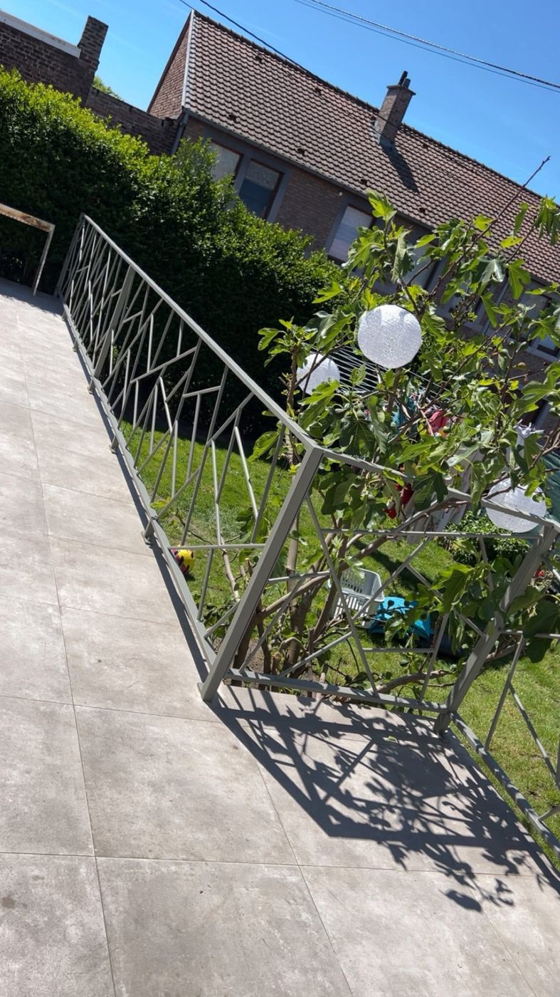 Long garde-corps de terrasse gris au motif géométrique, le long d'un jardin