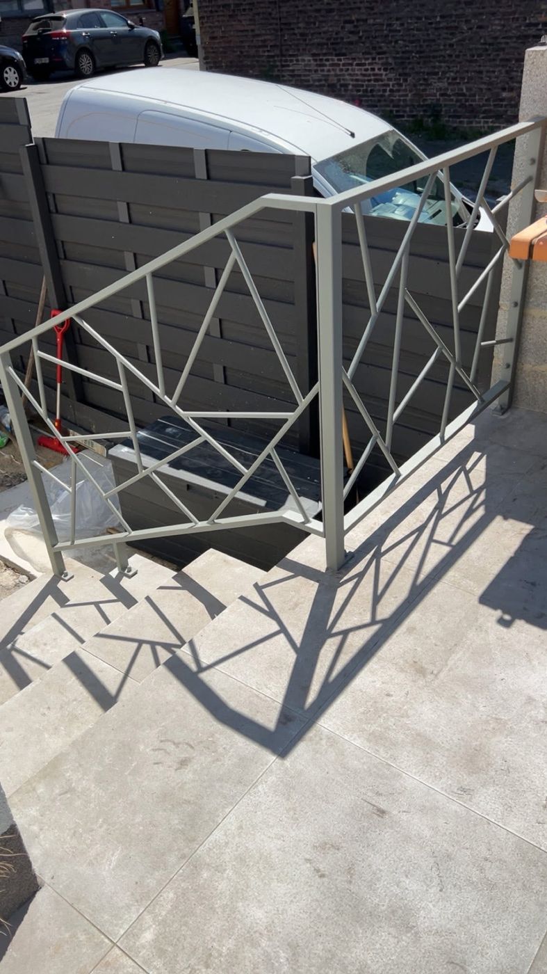 Rampe d'escalier extérieur grise au motif géométrique, dont l'ombre se dessine sur les marches